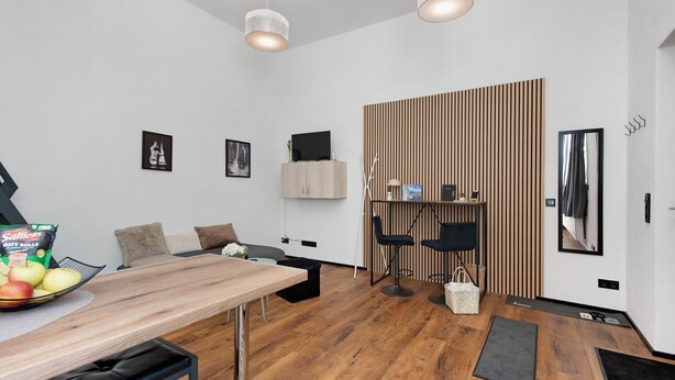 A modern room with a wooden dining table, black chairs, a sofa, a TV, and a wooden slat partition.