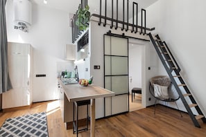 A modern kitchen with a wooden table, a black chair, and a staircase.