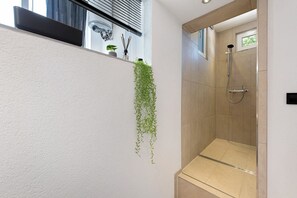 A modern bathroom with a shower, a hanging plant, and a window with blinds. - Apartment Myraybay near the Lake with Wi-Fi and Optional Swimming Area (Stockach)