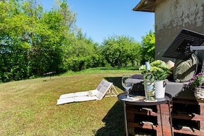 A grassy area with a lounge chair, a table with a bottle and glass, and a building with a brick wall and a metal structure.