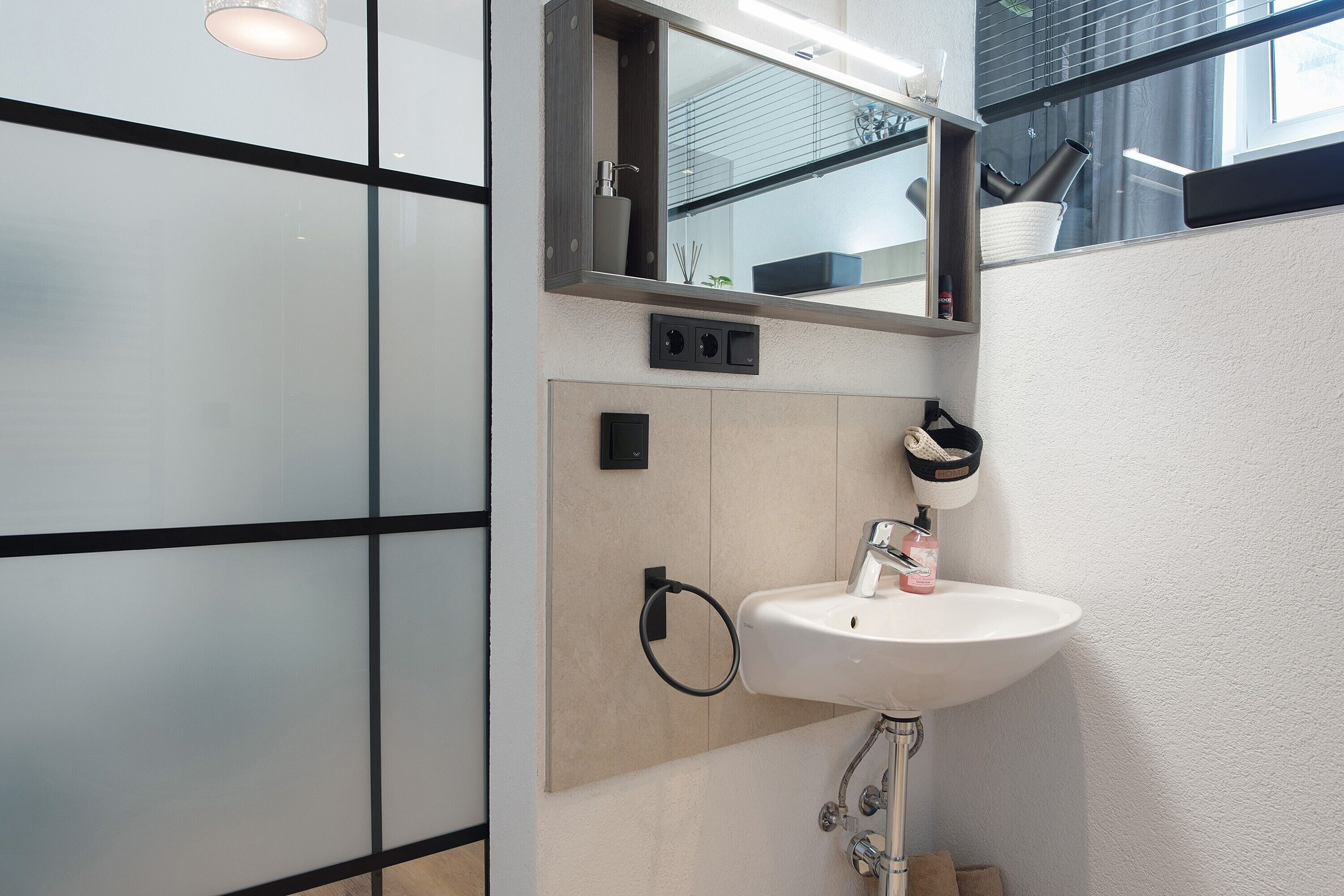 Un baño moderno con un lavamanos blanco, un espejo y un perchero para toallas.