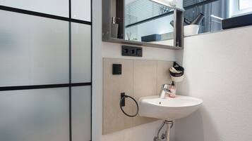 Un baño moderno con un lavamanos blanco, un espejo y un perchero para toallas.