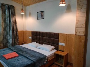Un dormitorio con cabecera de madera, una cama con ropa de cama blanca, una mesita de noche y un velador.