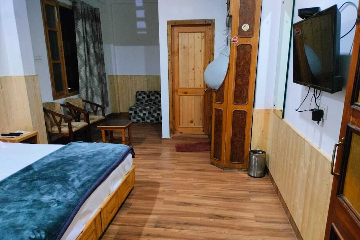 Una habitación con cama, puerta de madera, televisor y una mesita.