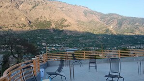 A terrace with metal chairs and tables, overlooking a mountainous landscape with scattered buildings.