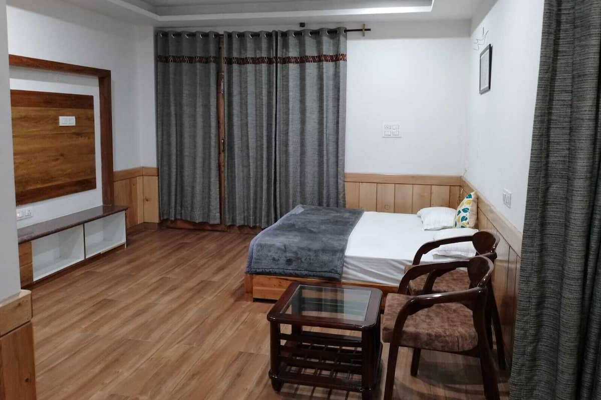 Habitación de hotel con cama, una mesita, una silla, televisor y armario.