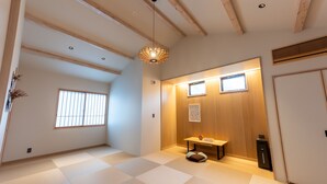 Una habitación con suelo de tatami, techo de madera, lámpara colgante, una pequeña mesa con cojín y una puerta corrediza.