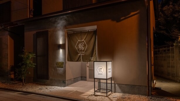 Entrada de un hotel con un cartel que muestra el nombre 'UGI SUI' y un logotipo.