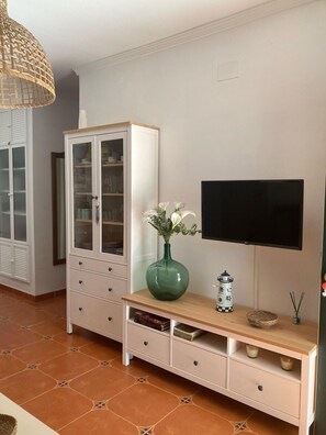 Ein Wohnzimmer mit Fernseher, einer Vitrine, einer Vase mit Blumen und einer kleinen Leuchtturm-Dekoration.