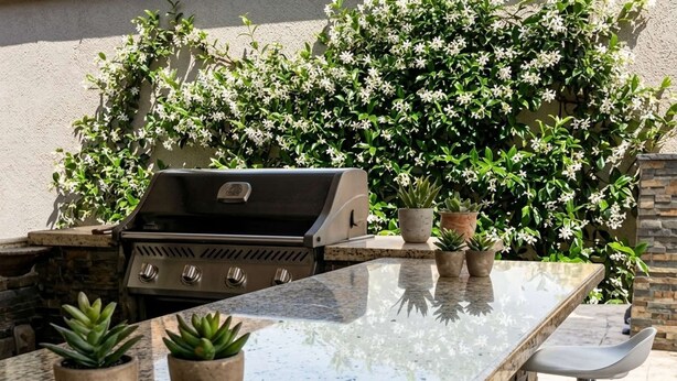 An outdoor kitchen with a grill, potted plants, and a bar area.