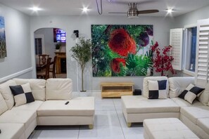 A living room with two beige sofas, a wooden coffee table, a large floral painting, and a ceiling fan.