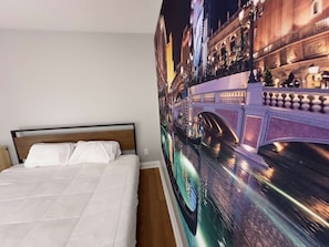 A hotel room with a bed, a wall mural of a canal, and a bridge.
