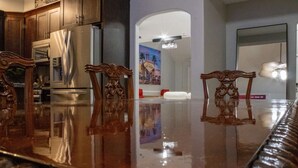 A dining area with a reflective polished table, wooden chairs, and a view of a hallway with a poster.