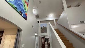 A modern interior with a staircase, a hallway leading to a dining area, and a painting on the wall.