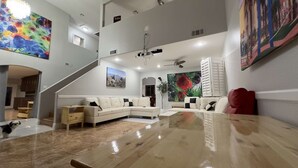 A spacious living area with a large wooden coffee table, a white sectional sofa, and a staircase leading to an upper level.