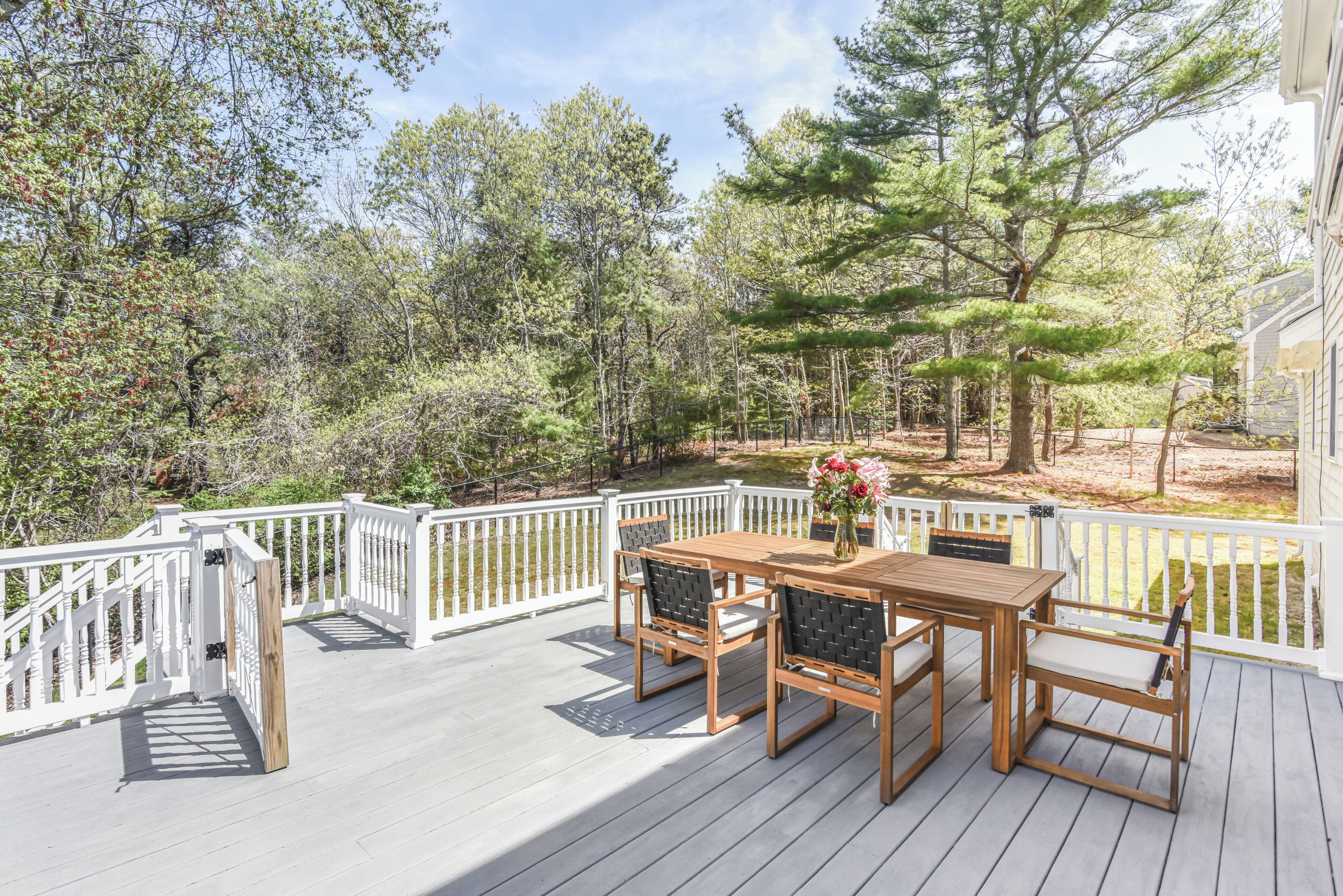 A wooden deck with a white railing, surrounded by trees and a clear sky.