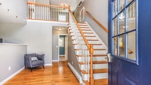 Un interior espacioso con una escalera de madera, una puerta azul y un sillón gris.