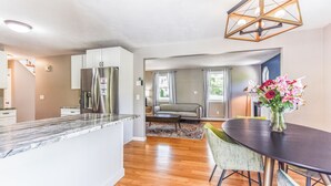 Una cocina moderna con un refrigerador de acero inoxidable, un comedor con una mesa oscura y sillas verdes, y una sala de estar con un sofá y una mesa de centro.