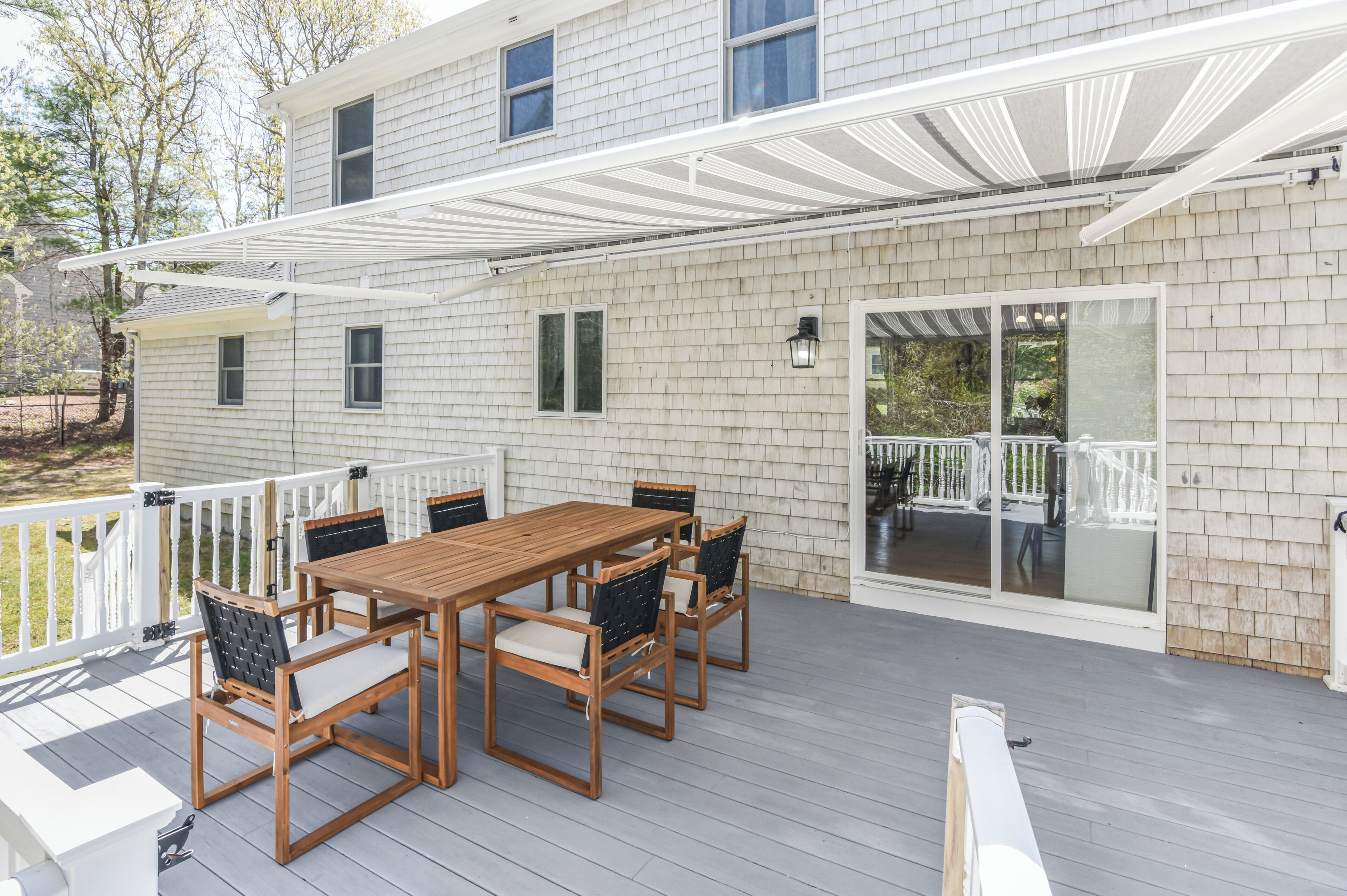 A covered patio with a wooden table and chairs, a white railing, and a sliding glass door leading to an outdoor area.