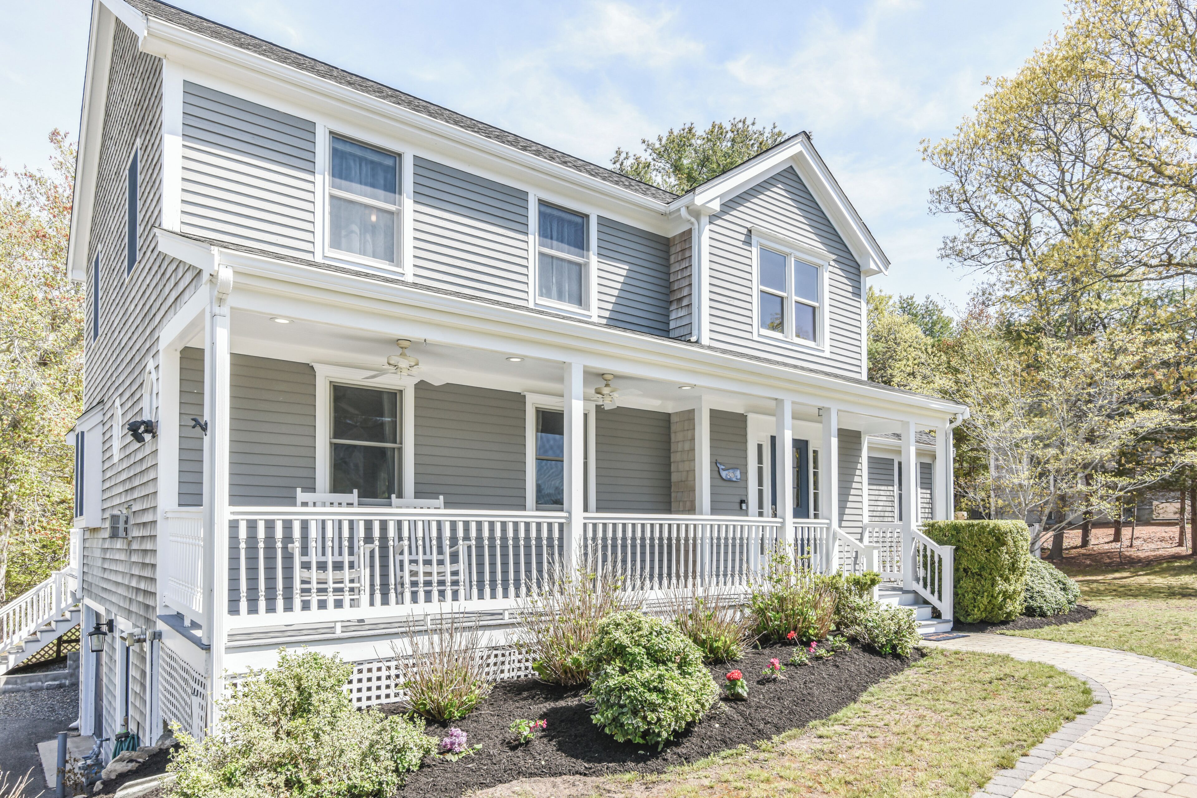 A two-story house with a covered porch, a front yard with various plants, and a pathway leading to the entrance.
