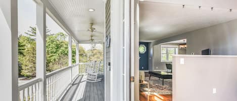 A covered porch with a ceiling fan, a view of the outdoors, and a room with a desk and chair.