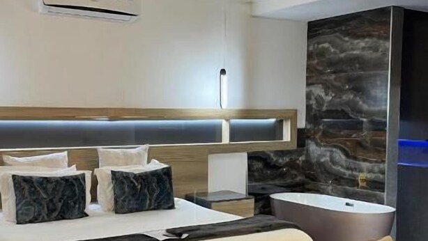 A modern hotel room with a bed, a sofa, a desk, and a large stone wall. - Room-17 On Buffalo Sandton (Johannesburg)