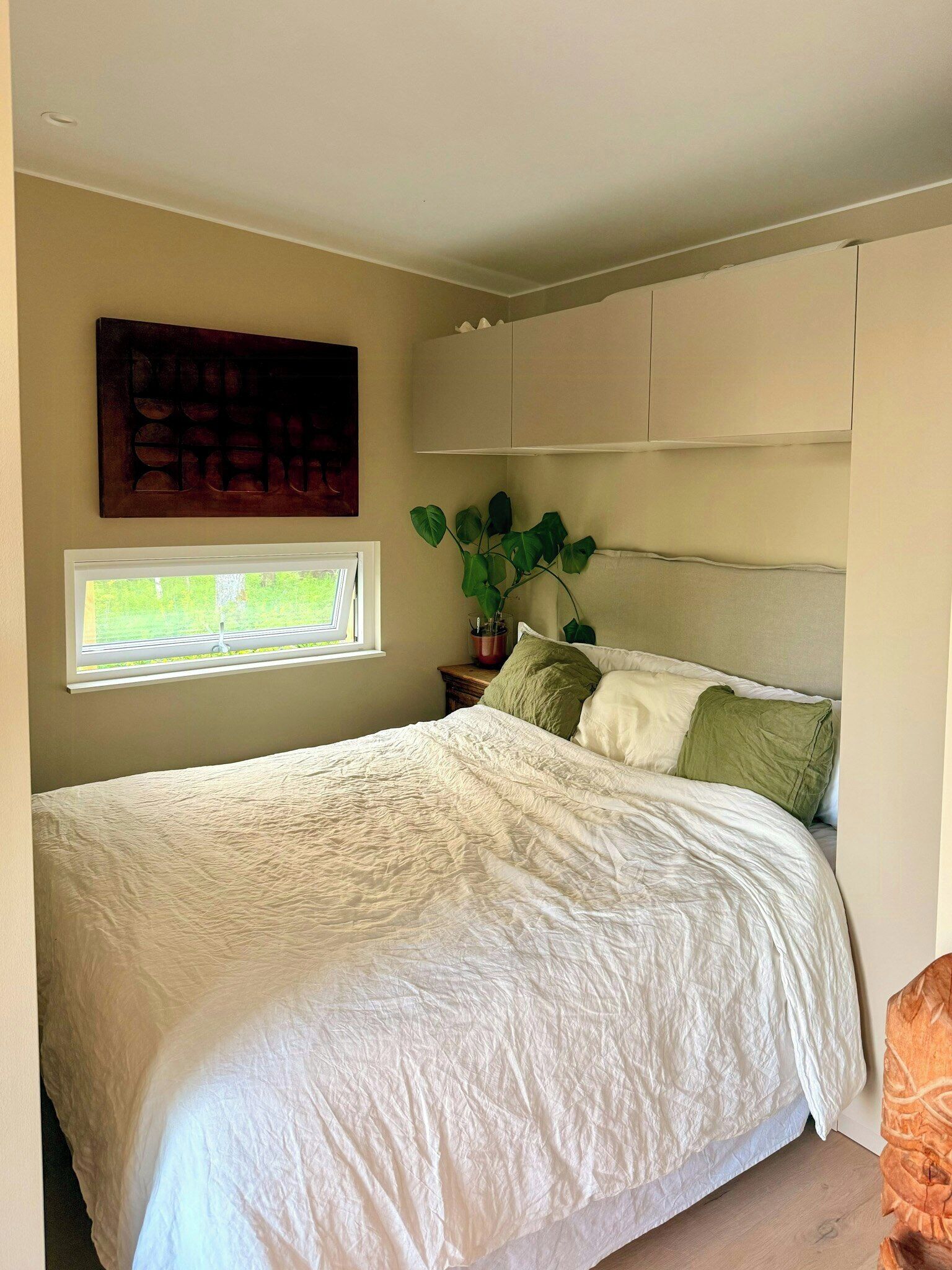 Una camera da letto con un letto, una finestra, una pianta e un quadro appeso al muro.
