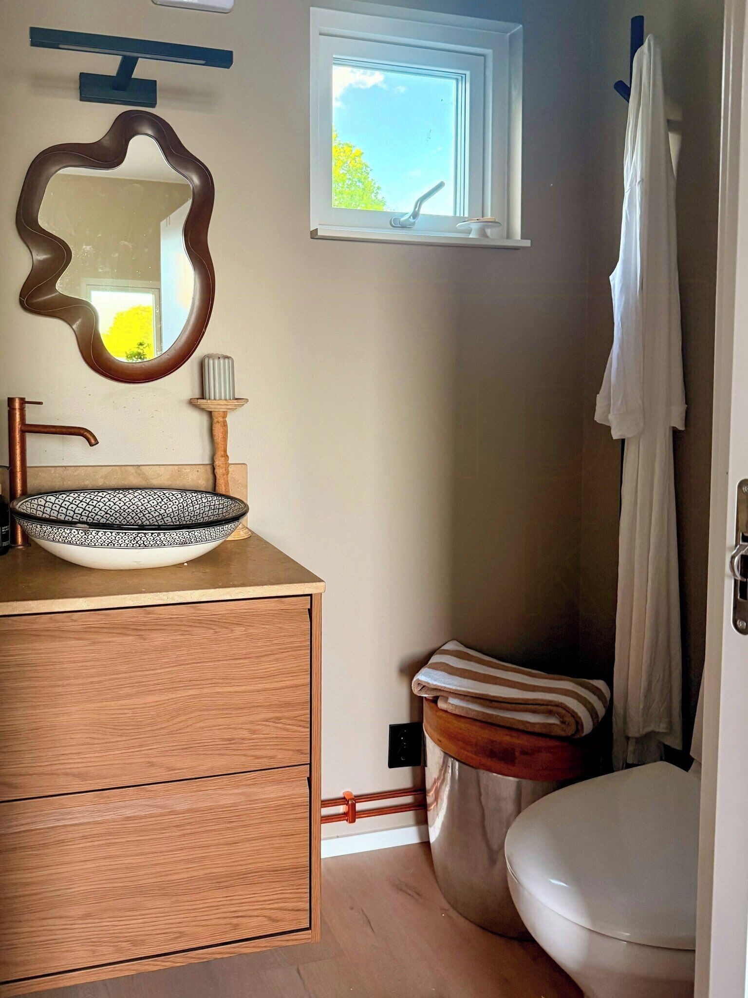 Un bagno con un mobile bagno in legno, un lavabo a incasso, uno specchio, una finestra, un water e un porta asciugamani.