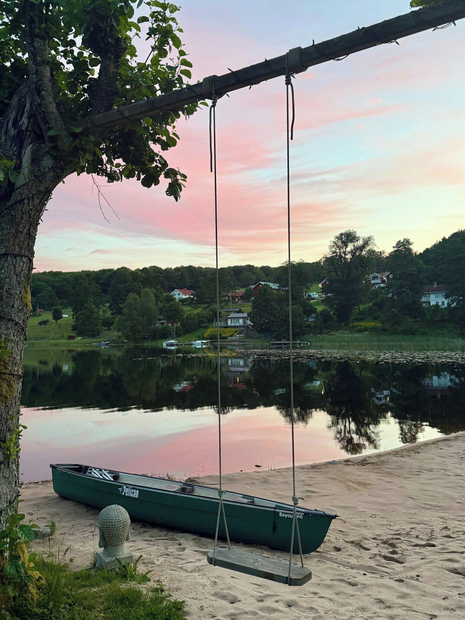 Uno scenario tranquillo sul lago con un’altalena, una barca e case sullo sfondo.