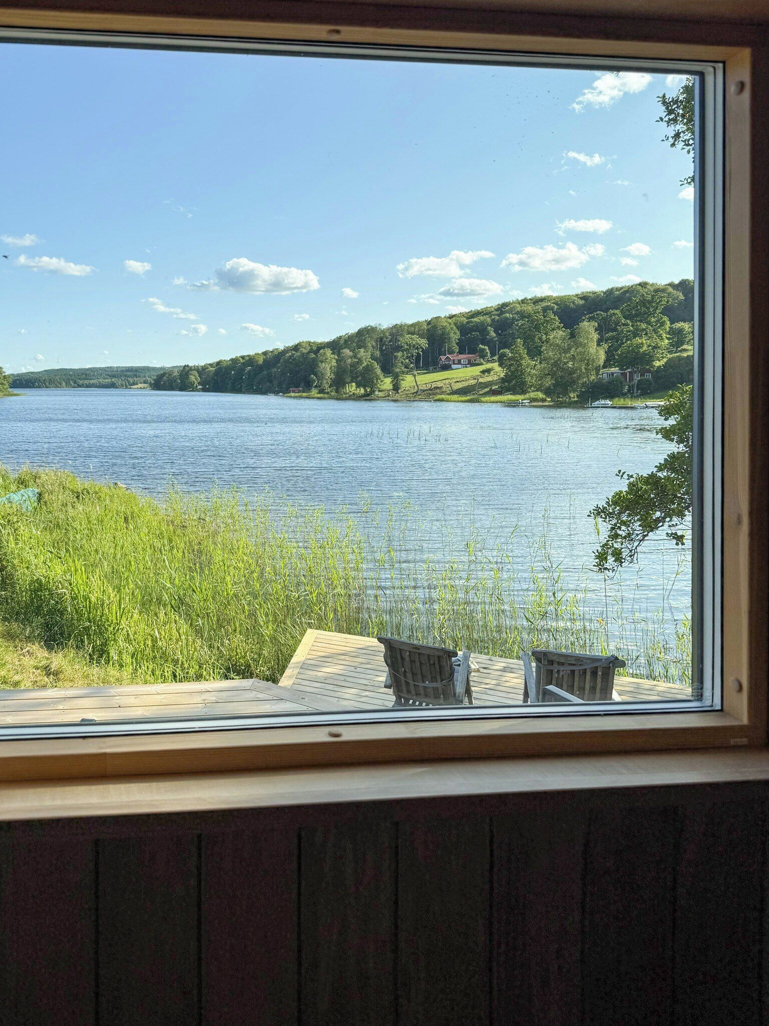 Vista al lago desde una ventana, con dos sillas de madera en una terraza.