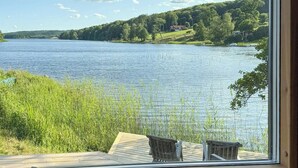 En utsikt över sjön från ett fönster, med två trästolar på en veranda.