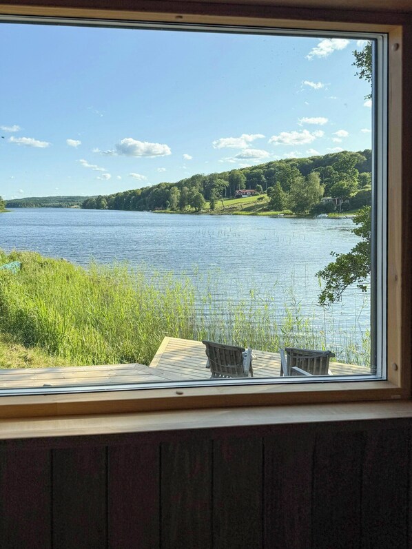 Uitzicht op een meer vanaf een raam, met twee houten stoelen op een terras.