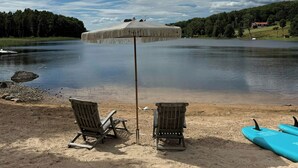 En strand vid en sjö med två solstolar, ett parasoll och en kajak.