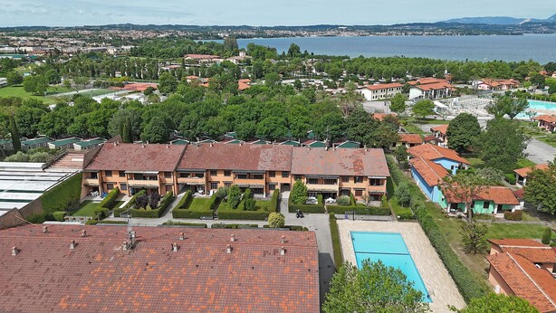 Zona residencial con un gran edificio que tiene piscina, rodeado de vegetación y vista al lago.