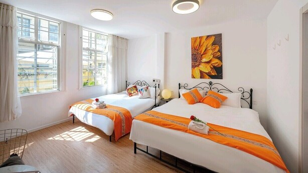 Una habitación de hotel con dos camas, un ventanal grande, un cuadro y una lámpara en el techo.