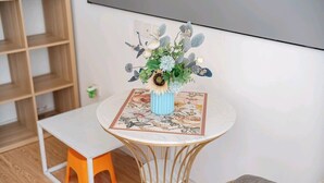 Una pequeña mesa redonda con un jarrón azul lleno de flores, una silla blanca y una estantería de madera al fondo.