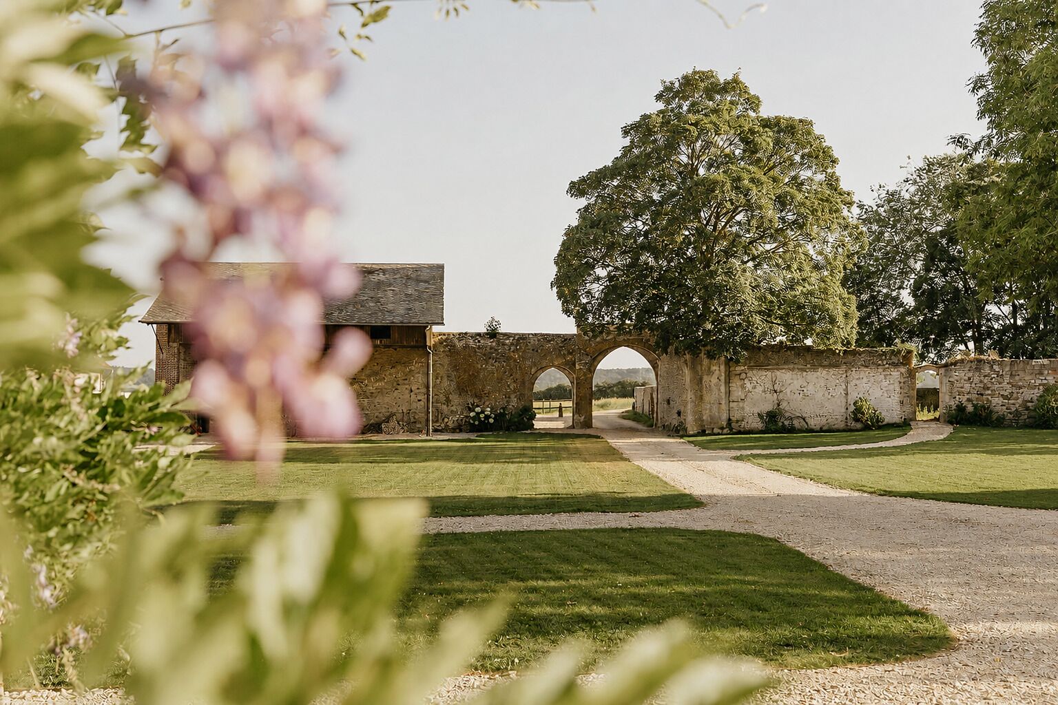 Un arc en pierre qui mène à un bâtiment, entouré d’une pelouse et d’arbres bien entretenus.