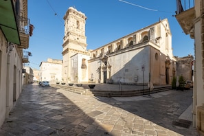 A historic building with a prominent tower, a courtyard with steps, and a paved street.
