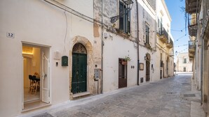 A narrow cobblestone street with buildings on either side, a green door, and a number '12' sign.