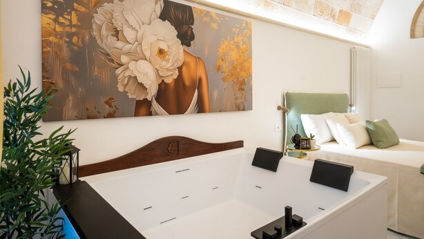 A modern bedroom with a large painting, a bed, a bedside table, and a plant.