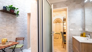 A modern interior with a stone wall, a dining area with a table and chairs, a sliding glass door leading to a bathroom, and a hexagonal tiled wall.