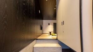 Un pasillo con pared de madera, suelo alfombrado y una escalera que lleva a una habitación con una mesa redonda y un cojín verde.