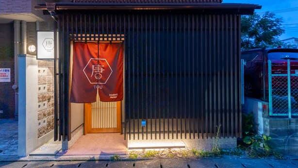 Entrada de hotel con puerta de madera, un letrero con caracteres japoneses y una reja metálica.
