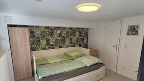 Ein Schlafzimmer mit Bett, Kleiderschrank, Tür und Wand mit Pflanzenmuster.