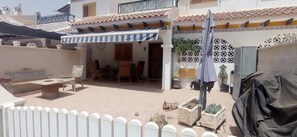 Une cour dotée d’un espace de repos abrité, de plantes en pot et d’un toit recouvert de tuiles.
