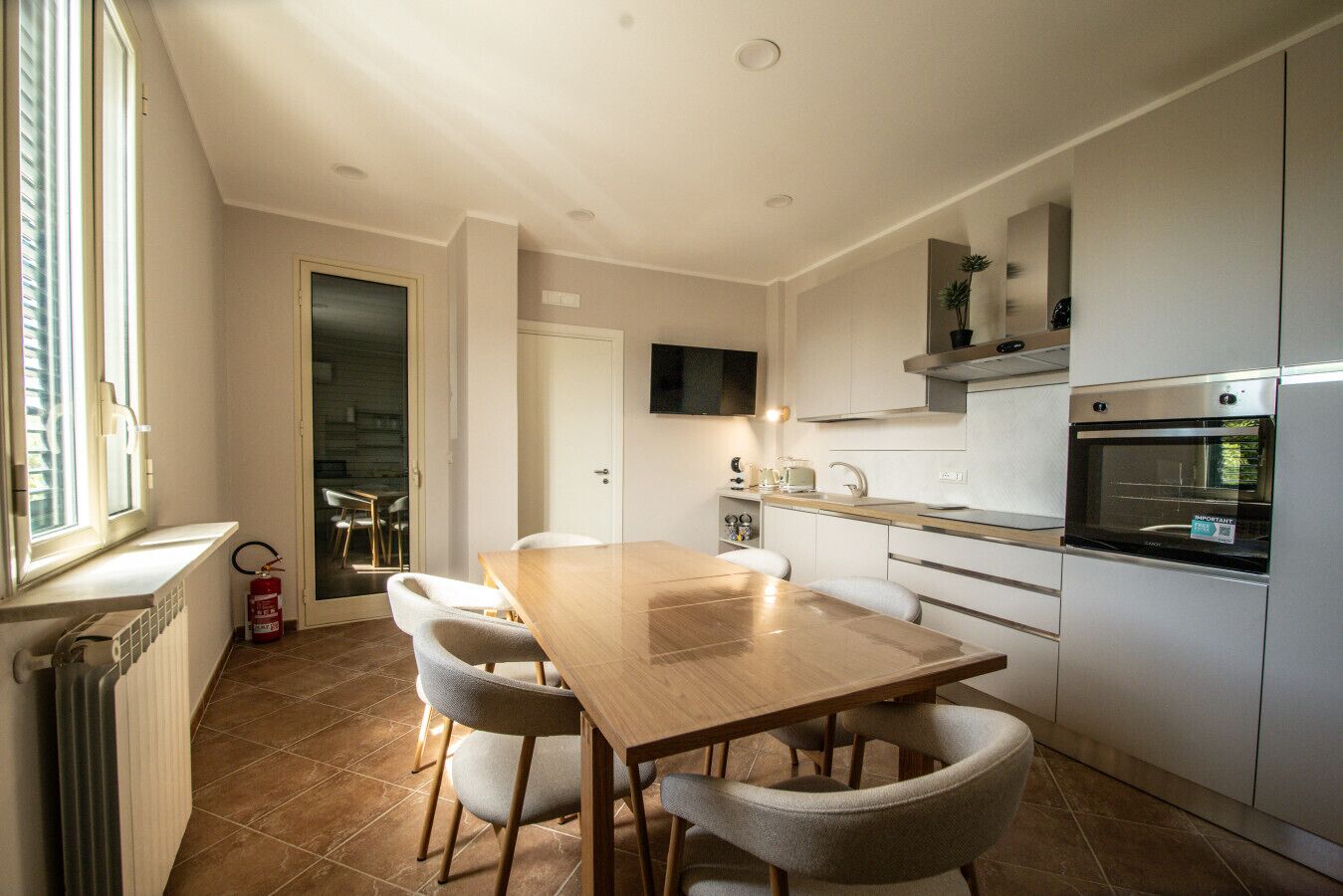 A modern kitchen with a wooden table and chairs, a built-in oven, and a TV mounted above the counter.