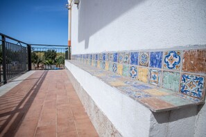 Un vialetto esterno piastrellato adiacente a un muro bianco con ringhiera in metallo nero.