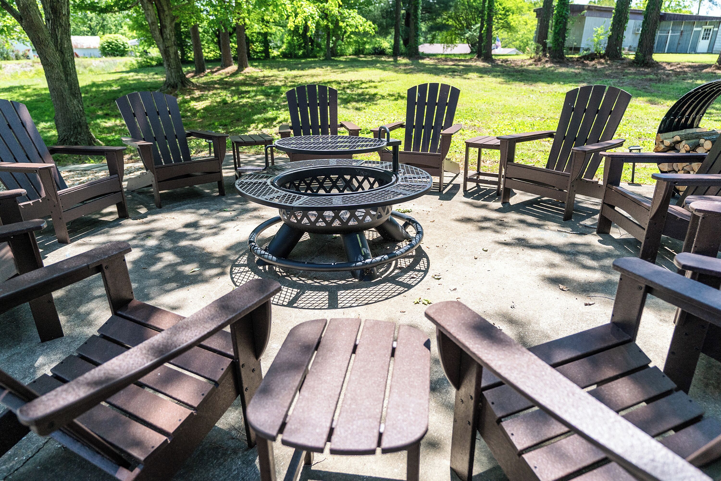 A circular fire pit table surrounded by Adirondack chairs in an outdoor setting.