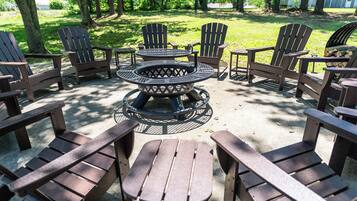 A circular fire pit table surrounded by Adirondack chairs in an outdoor setting.