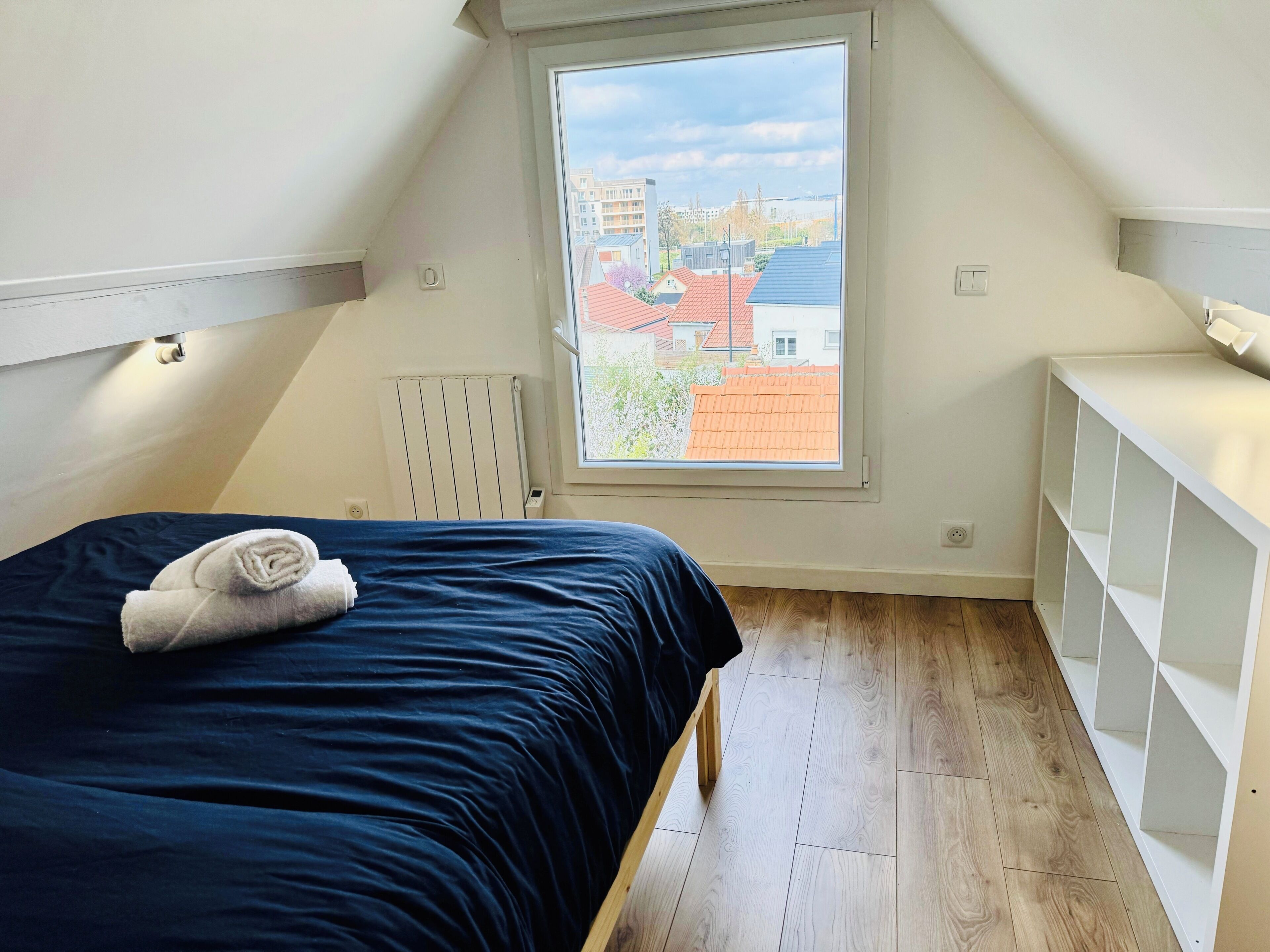 Une chambre à coucher avec un lit, un radiateur, une fenêtre et une étagère blanche.